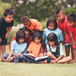 group-of-children-lying-reading-on-grass-field-PHDSSH8